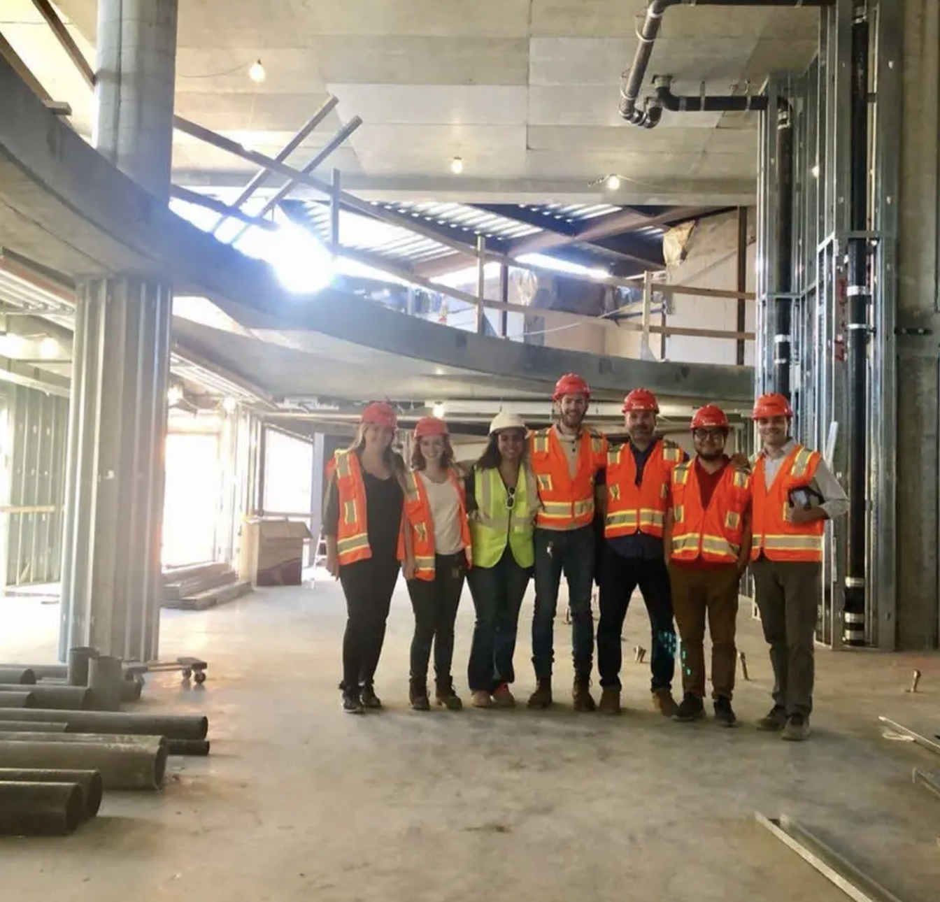 Construction consultants in orange vests gathered inside a building under construction